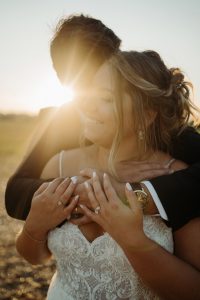 Groom hugging bride from behind at sunset