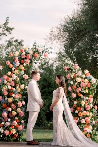 Bride and Groom standing in front of colourful floral archway at their ceremony