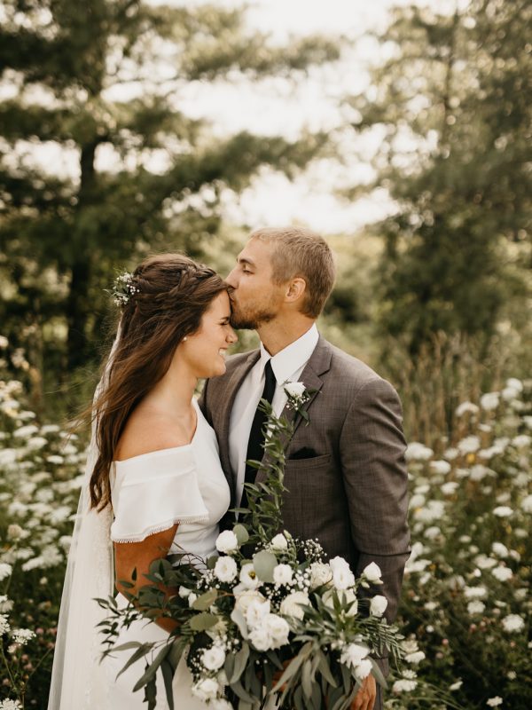 Groom kissing brides forehead in forest