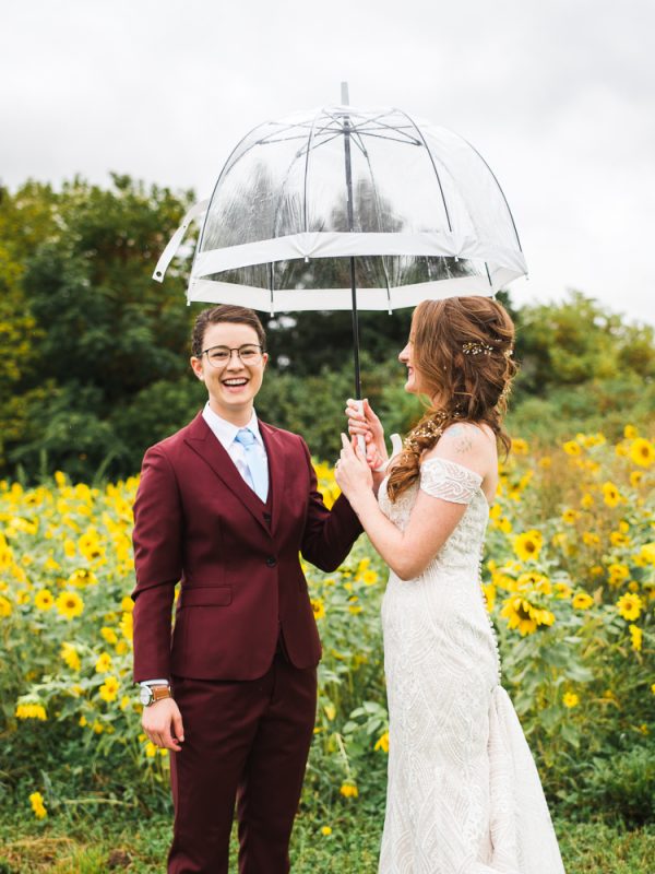 Two women on their wedding day in a sunflower field holding umbrella
