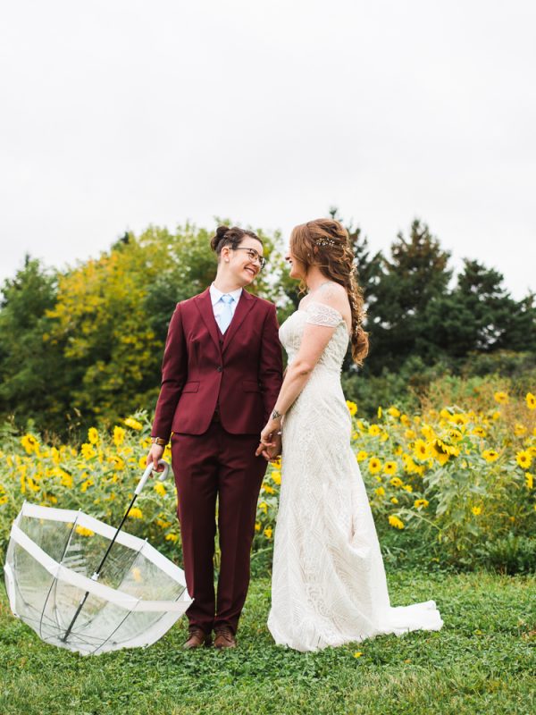Two women on their wedding day holding umbrella in sunflower feild