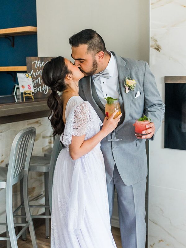 Bride and groom holding signature cocktails while kissing