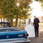 Wedding couple walking into sunset with old blue car beside