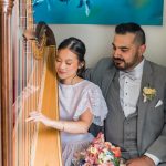 Bride playing harp with groom sitting beside